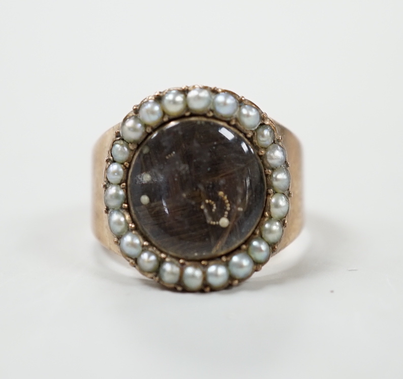 A George III yellow metal mourning ring, with plaited hair beneath a glazed panel and seed pearl set border, the back inscribed 'Mr. James Glover obt, 20th Jan, 1792 at 53', size H, 3 grams.